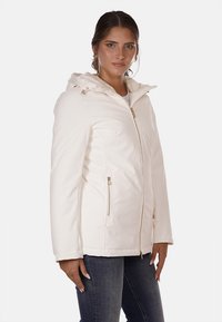 Giacca bianca isolante con cappuccio, dotata di chiusura con zip, tasche laterali e accessori in tonalità dorata. Tessuto liscio e leggero.