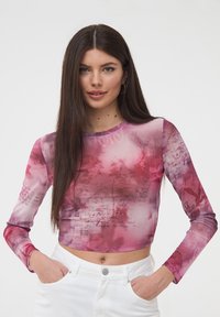 Top corto a maniche lunghe in un tessuto rosa trasparente, caratterizzato da un motivo floreale e testo scritto a mano, con un collo rotondo e una silhouette aderente.