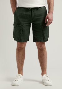 Dunkelgrüne Cargo-Shorts aus strukturiertem Stoff, mit Seitentaschen und einem Kordelzugbund. Getragen mit weißen Turnschuhen.