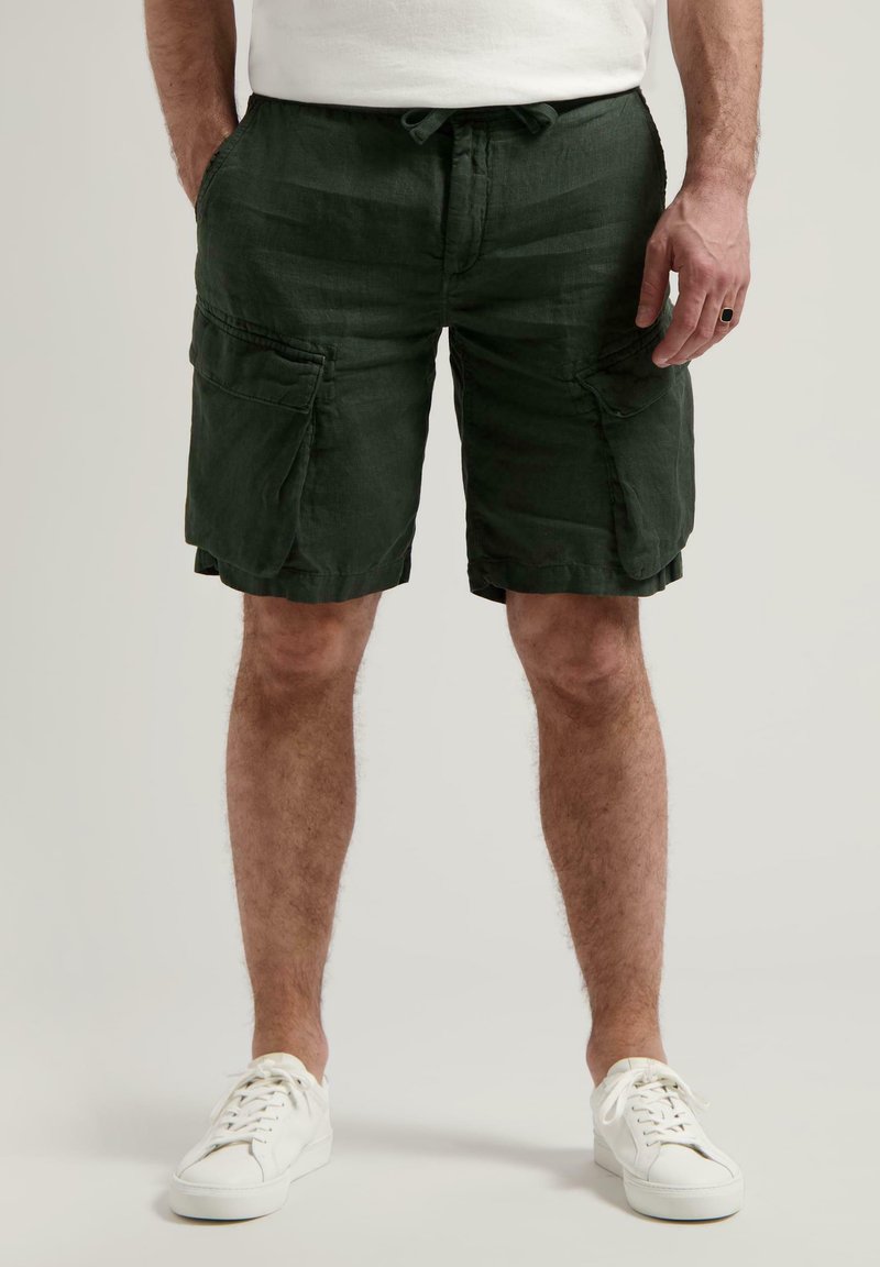 Dunkelgrüne Cargo-Shorts aus strukturiertem Stoff, mit Seitentaschen und einem Kordelzugbund. Getragen mit weißen Turnschuhen.