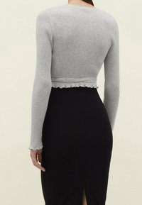 Maglione grigio a coste corto con maniche lunghe, dotato di orlo arricciato, abbinato a una gonna nera aderente con uno spacco laterale.