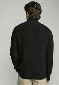 Schwarzer Strickpullover mit hohem Kragen, gerippter Textur und langen Ärmeln. Die Rückseite hat eine glatte Oberfläche und ist klassisch geschnitten.