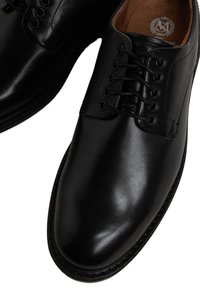 Chaussures en cuir noir avec une finition brillante, présentant un design classique à lacets, des coutures robustes et une texture lisse.