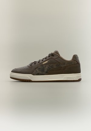 Κοντό αθλητικό παπούτσι Puma από σκούρο καφέ δέρμα με υφασμένο πλαϊνό λωρίδα και λευκή σόλα σε ουδέτερο φόντο.