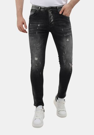 Zwarte verouderde skinny jeans met vervaagde plekken, met een klassieke vijf-pocket stijl. Draagt men met witte sneakers.