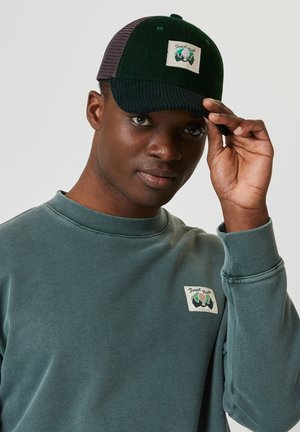 Dark green cap with a textured brim, featuring a white square patch with "Forest Night" and a mountain logo. Gray fabric on the back.