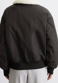 Czarna kurtka bomberka z białym kołnierzem ze sztucznego kożucha, ściągaczami na mankietach i u dołu, o gładkim wykończeniu i luźnym kroju.