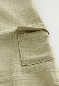 Tissu en lin vert clair avec une surface texturée. Dispose d'une petite poche plaquée et de coutures visibles le long des bords.