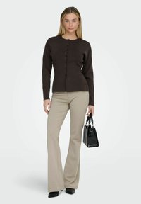 Cardigan marron foncé à col rond et boutons sur le devant, associé à un pantalon beige évasé et un petit sac noir embossé effet croco.