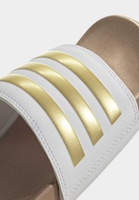 Sandalo bianco con tre strisce metalliche dorate sulla parte superiore, con un plantare marrone effetto texture e bordi lisci.