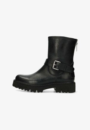 Botines de cuero negro con puntera ancha, una correa con hebilla y una suela de goma gruesa con surcos profundos. Cierre con cremallera en el lateral.