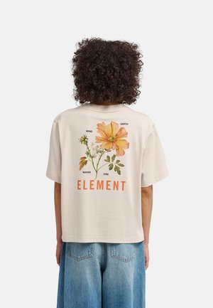 Persoon met krullend haar die een beige T-shirt draagt met een grote oranje bloem en de woorden Aarde, Wind, Water, Vuur en Element op de achterkant.