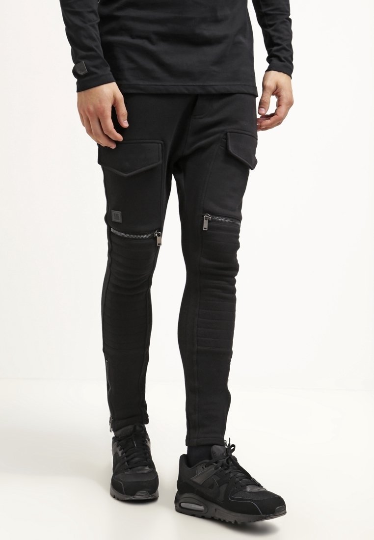 Svarta joggingsbyxor i stretchmaterial, med dragkedjefickor, ribbade knädetaljer och en smal passform. Bärs med svarta sneakers.