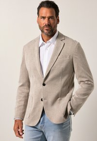 Beige houndstooth-takkia, jossa on kaksi etutaskua, yksinäinen nappisulku ja lovet; yhdistetty valkoiseen paitaan ja vaaleisiin farkkuihin.