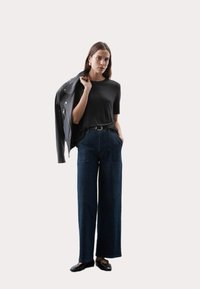 Zwarte top met korte mouwen, hooggelegen wijde spijkerbroeken van donkerdenim en een zwart leren jack over één schouder gedrapeerd. Zwarte ballerina's met accenten.