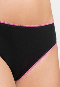Bikini in cotone nero con bordo ondulato rosa lungo la vita, caratterizzato da una texture liscia e un design semplice.