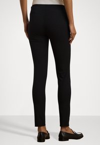 Zwarte legging gemaakt van rekbare stof, met een slim fit ontwerp, een gladde textuur en een middenhoog taille, gecombineerd met zwarte instappers.