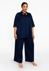Navyblauwe twee-delige outfit bestaande uit een losse blouse met een keyhole halslijn en vloeiende broekspijpen, gemaakt van een gladde, lichte stof.