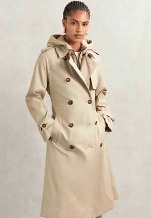 Trench coat beige con cappuccio, design doppiopetto, grandi bottoni marroni e tasche laterali. Tessuto robusto con una texture liscia.