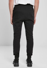 Fekete, testhez simuló szabadidőnadrág puha anyaggal, rugalmas derékpánttal és egy hátsó zsebbel; fekete lábbelivel párosítva.