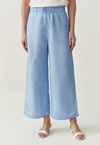 Lichtblauwe, wijde broek van een gestructureerde stof met een elastische tailleband en een koord. Beschikt over zijzakken en een ontspannen pasvorm.
