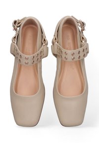 Des chaussures beiges avec un design à bout carré, dotées d'une large sangle avec des œillets en ton doré et une fermeture à boucle. Texture lisse sur l'ensemble.