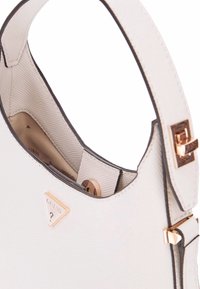 Borsa a tracolla bianca testurizzata con una parte superiore curva e dettagli in ottone. Presenta un logo visibile e una tasca interna. Fodera interna liscia.
