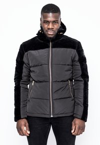 Svart puffjacka med en strukturerad svart sammetspanel, dragkedja framtill, sidfickor och huva. Slim fit med quiltade paneler.