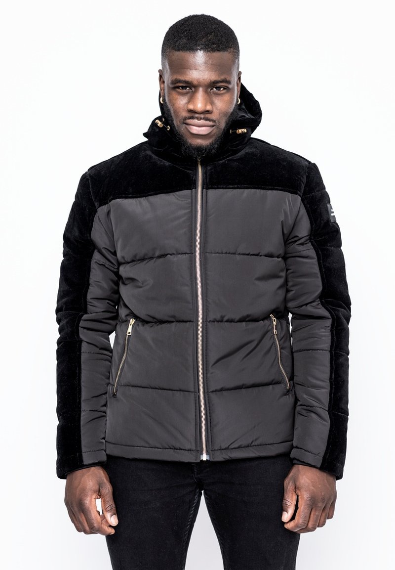 Svart puffjacka med en strukturerad svart sammetspanel, dragkedja framtill, sidfickor och huva. Slim fit med quiltade paneler.