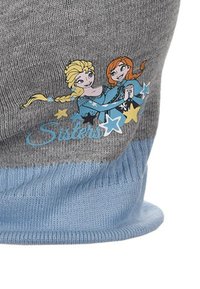 Gorro de punto gris con ribete azul que presenta un gráfico de dos personajes femeninos animados con estrellas y el texto "Hermanas" en azul claro.