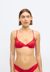 Czerwony koronkowy biustonosz z fiszbinami i regulowanymi ramiączkami, zdobiony kwiatowymi wzorami i falistymi krawędziami, do kompletu z dopasowanymi koronkowymi majtkami.