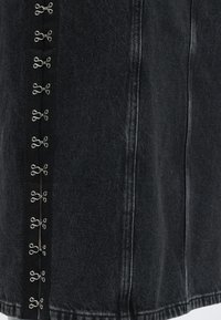 Μαύρο denim ύφασμα με κάθετες μεταλλικές κλειδαριές γάντζου και ματιού κατά μήκος μιας ραφής, που δείχνει υφή και λεπτομέρειες ραφής.