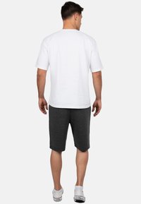 Witte T-shirt met korte mouwen en grijze shorts, gedragen door een mannelijke figuur. Het T-shirt heeft een ronde hals, en de shorts zijn knielang met een ontspannen pasvorm.