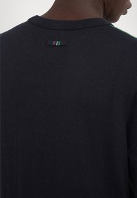Navy blue sweater with a ribbed texture, featuring a crew neck and a small multicolored tag at the back. Simple design, no embellishments.