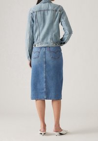 Chaqueta de denimbl azul claro con un diseño ajustado y dos bolsillos en el pecho, combinada con una falda de denimbl azul claro hasta la rodilla. Textura suave.