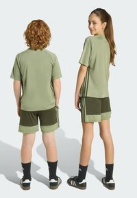 Green athletic outfit featuring short-sleeved shirt and shorts with contrasting olive panels. Includes three white side stripes and black socks.