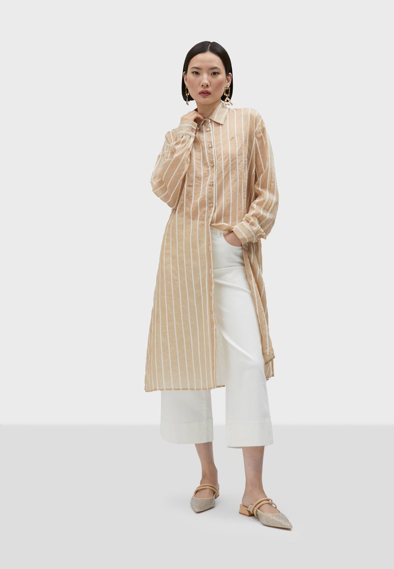 Beige randig lång skjorta med avslappnad passform, kombinerad med vita cropped-byxor och utsmyckade slip-on-skor.