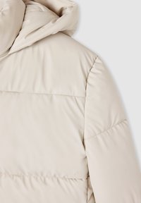 Kremowa kurtka puchowa z kapturem, pikowanym wzorem i widocznym szwem. Miękki, gładki materiał o lekko błyszczącym wykończeniu.