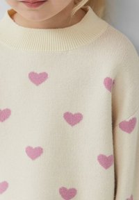 Gebreide trui met een ronde halslijn; crèmekleurig met verspreide roze hartmotieven; zachte textuur en een losse pasvorm.