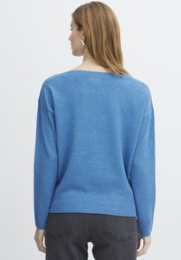 Pull en tricot bleu avec un large décolleté, coupe ample, et des poignets et un ourlet côtelés. Le tissu semble doux avec une finition légèrement texturée.