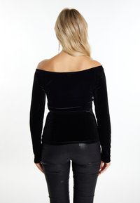 Sort fløjl off-the-shoulder top med lange ærmer, tætsiddende ved taljen, parret med skinnende sorte bukser, glat tekstur og elegant design.