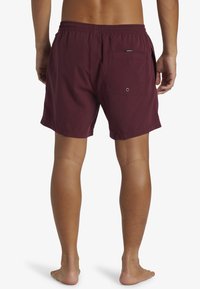 Pantalones de baño color marrón oscuro que cuentan con una cinturilla elástica, bolsillos laterales y traseros, y una tela suave y liviana para mayor comodidad.