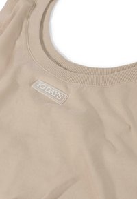 Top beige senza maniche con scollatura rotonda, realizzato in tessuto morbido. Presenta un colletto a coste texture e un'etichetta logo rettangolare.