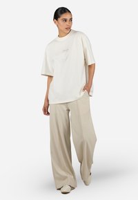 Cream oversized cotton t-shirt with short sleeves and a subtle embroidered logo, paired with loose-fitting beige trousers.