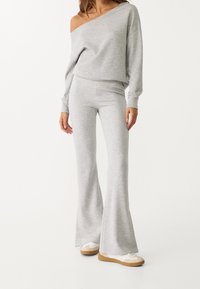 Light gray lounge set featuring an off-shoulder top and flared pants. Made of soft fabric with a cozy texture. Casual sneakers complete the look.