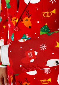 Costume rouge avec un motif festif comprenant des rennes, des sapins de Noël et des flocons de neige. Détails notables incluant des boutons rouges assortis et une étiquette de marque.