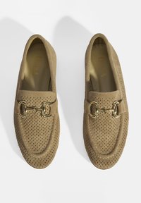 Braune Wildleder-Loafer mit perforiertem Obermaterial, goldfarbenen Hardware-Akzenten und gerundetem Zehenbereich. Glatte Innenauskleidung für Komfort.