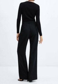 Czarny dopasowany sweter zestawiony z szerokimi spodniami w kolorze czarnym. Materiał wydaje się gładki, tworząc strawną sylwetkę z wysokim stanem.