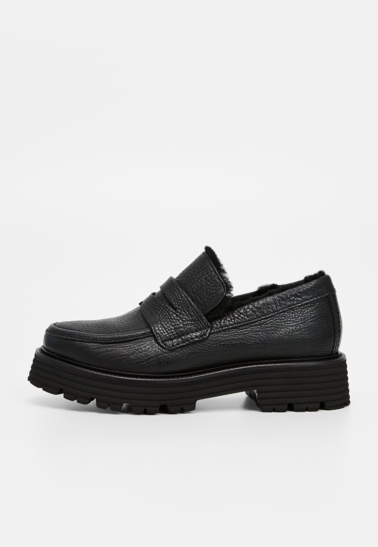 Schwarze Leder-Slipper mit strukturiertem Finish, ausgestattet mit einem breiten Riemen an der Oberseite und einer robusten, geriffelten Gummisohle.