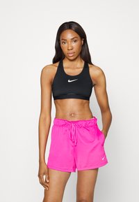 Μαύρος αθλητικός στηθόδεσμος και ροζ σορτσάκι κατασκευασμένα από λείο, ελαφρύ ύφασμα. Ο αθλητικός στηθόδεσμος διαθέτει λευκό λογότυπο, ενώ το σορτσάκι έχ�ει ελαστική μέση.